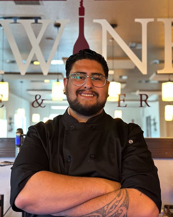 Chef Luis Contreras standing in front of a large wall mirror with the UnWINEd Wine & Beer Bar logo