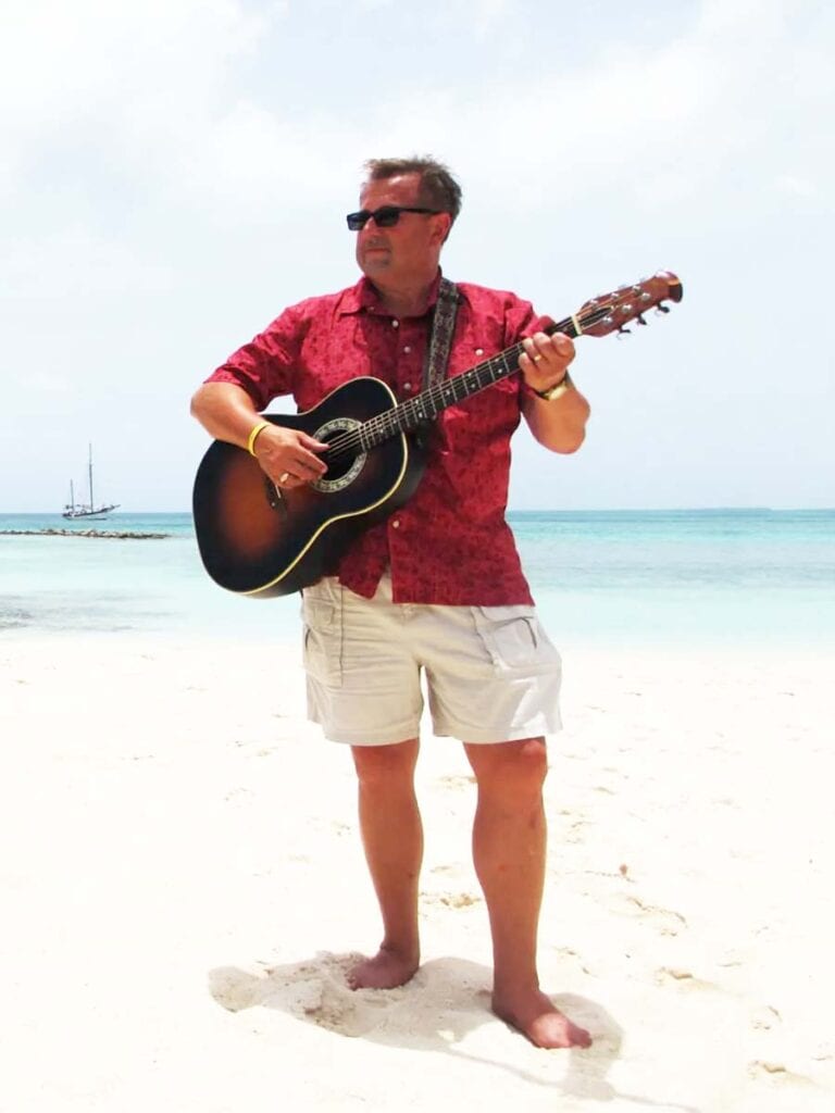 Musician Bob Schiele holding a guitar on the beach