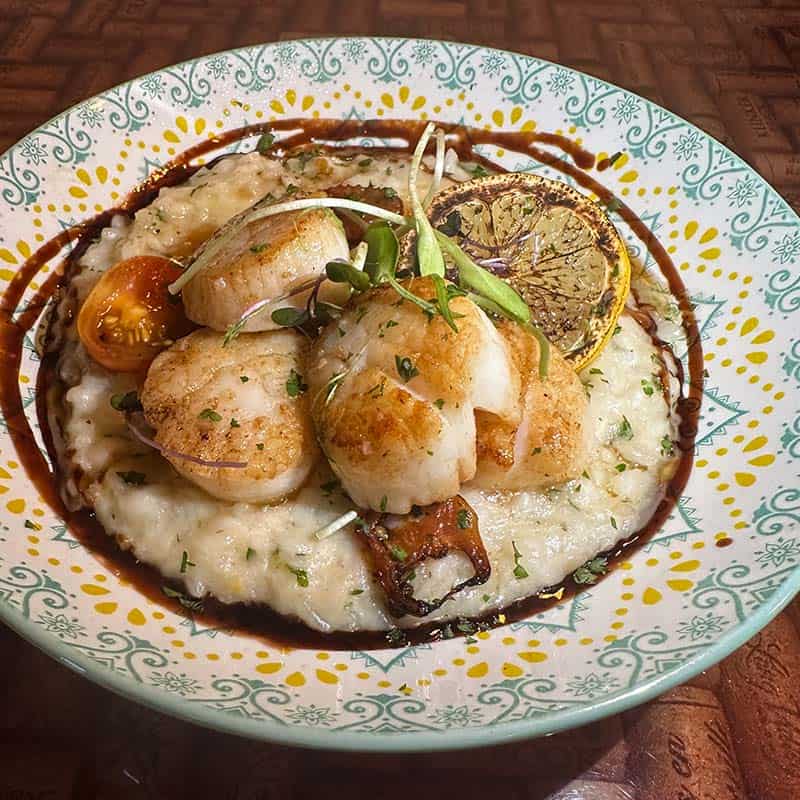 Four large, wild-caught pan seared scallops over lemon mascarpone risotto and roasted cherry tomatoes; topped with parmesan and smoked lemon zest